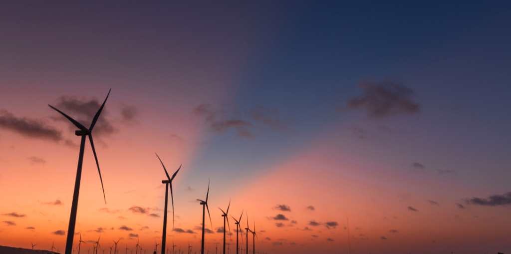 Aerogeradores de energia eólica em pôr-do-sol. Há 15 anos cruzando as fronteiras da energia. A Serena é pioneira em energia limpa, encurtando a distância entre consumidores e a melhor energia.